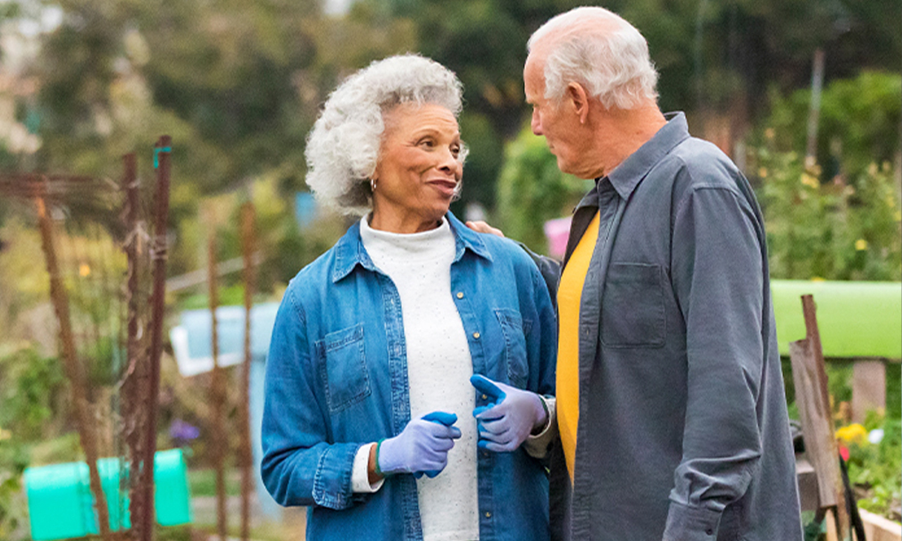 Female wearing a blue shirt and gloves speaking to a male while standing outside.