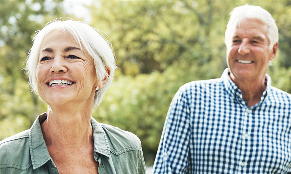 Elderly male and female standing outside smiling.