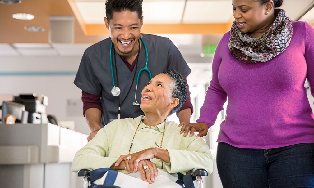 Elderly woman speaking to a doctor as she is pushed in a wheel chair.