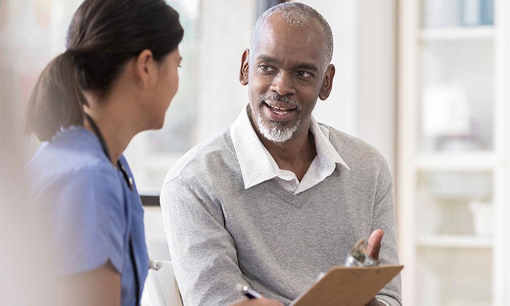 Male wearing a grey sweater speaking to a healthcare provider.