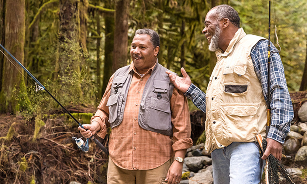 Two men standing outside talking. One of them is holding a fishing pole.